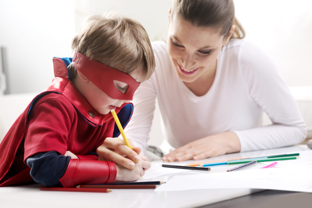 Speech therapist working with boy dressed in superhero costume, complete with red mask.